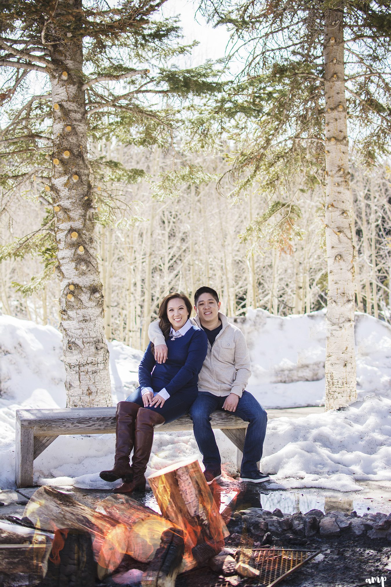 Engaged couple sitting beside bonfire surrounded by snow