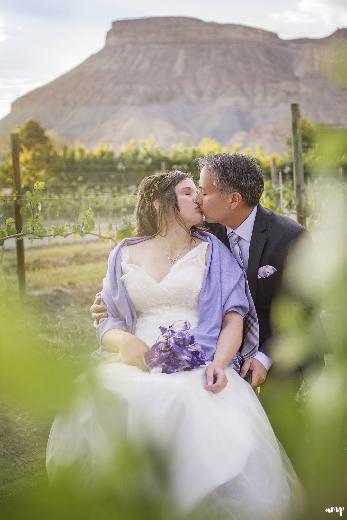 Couple kissing in a vineyard with Mt. Garfield in the distance