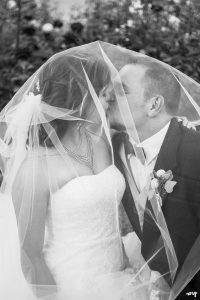 Bride and groom in black and white kissing beneath the veil