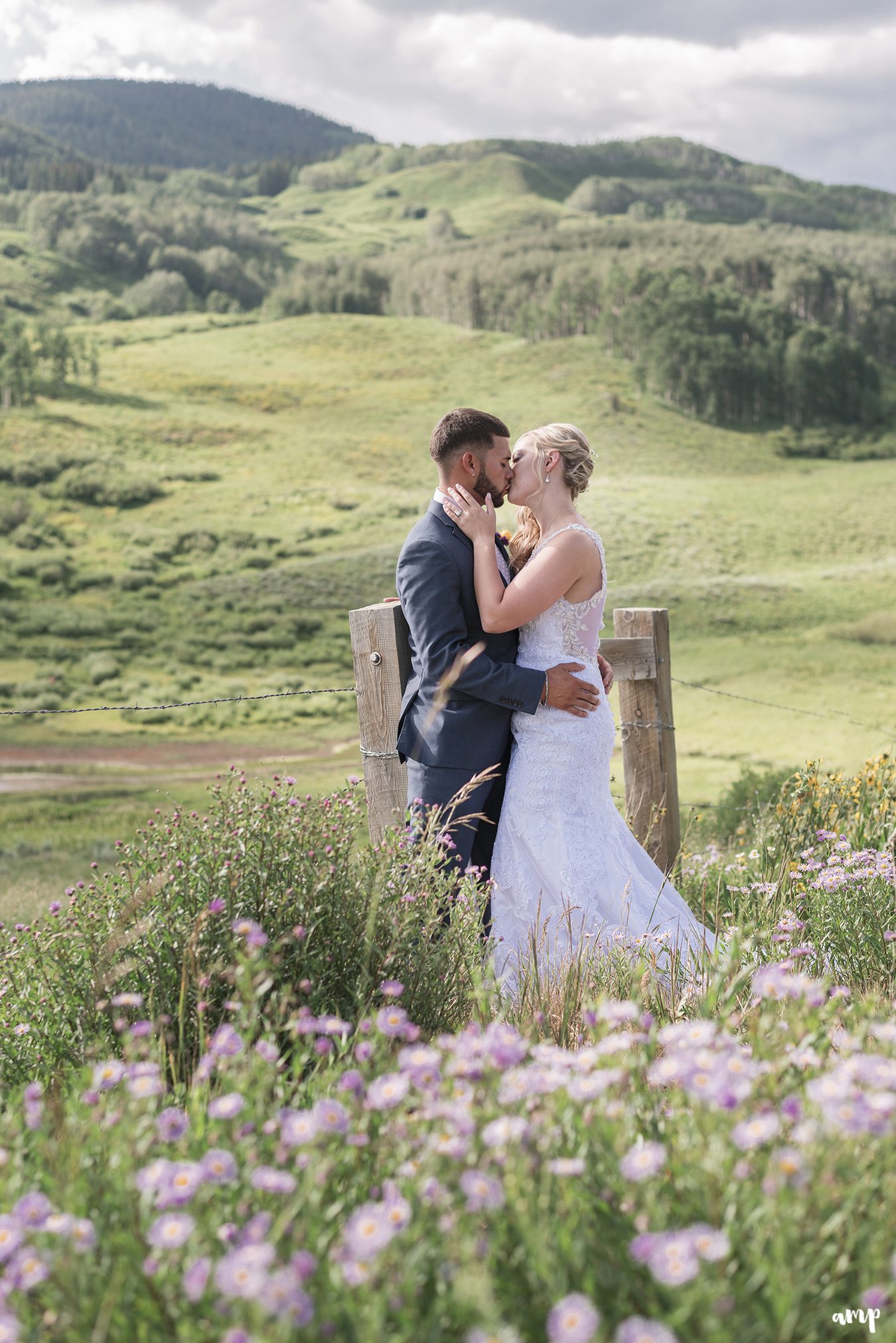 Bride and groom sharing a kiss among the wildflowers with mountains in the distance