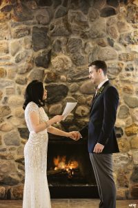 Bride and groom share vows in front of a fireplace