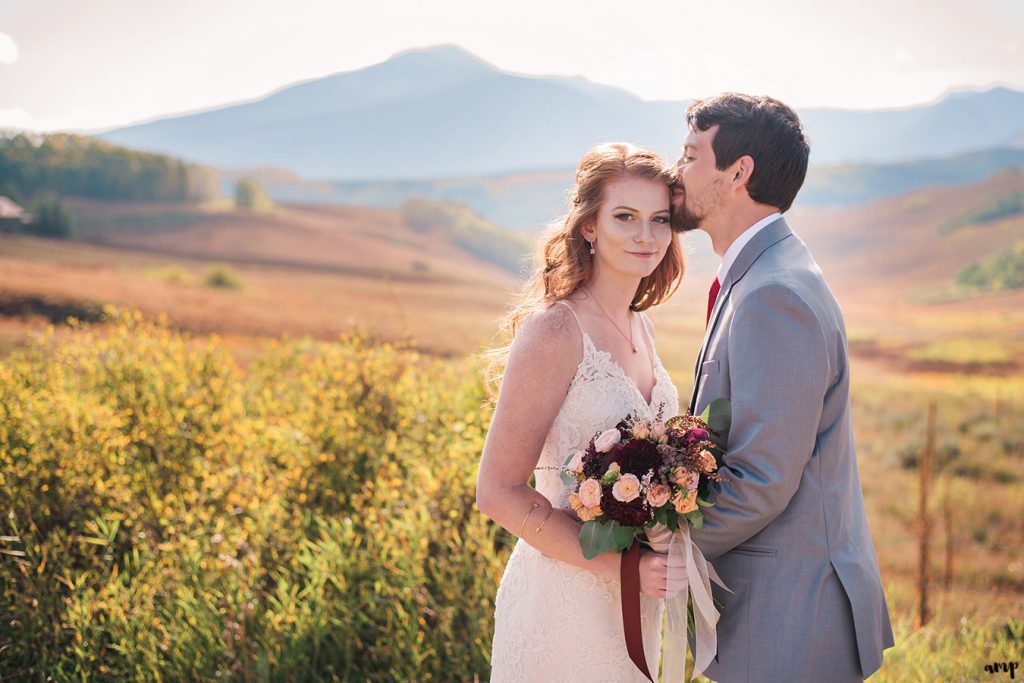 Bride and groom snuggling among the fall colors with mountains in the background