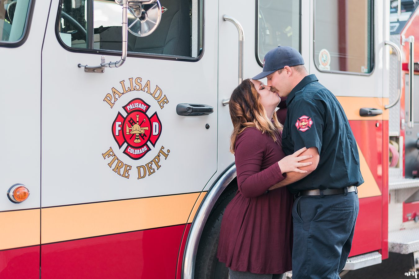 Engaged couple kissing in front of a fire engine