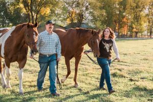 Engaged couple walking with their two horses at sunset