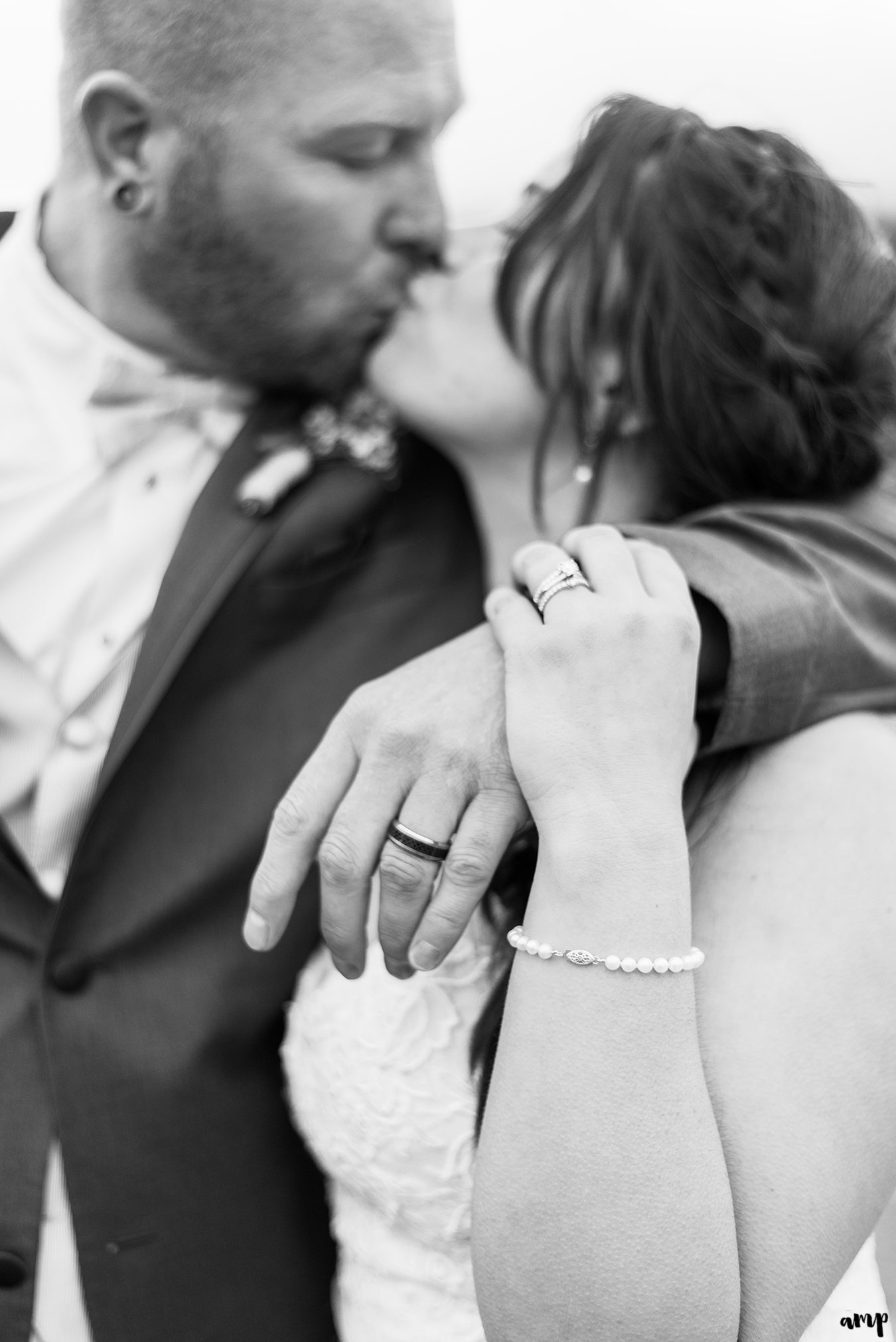 Black and white photo of bride and groom kissing, focused on the rings