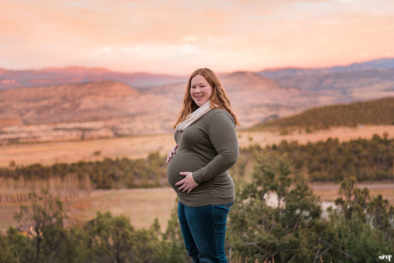 Pregnant woman holds her baby bump with mountains in the background