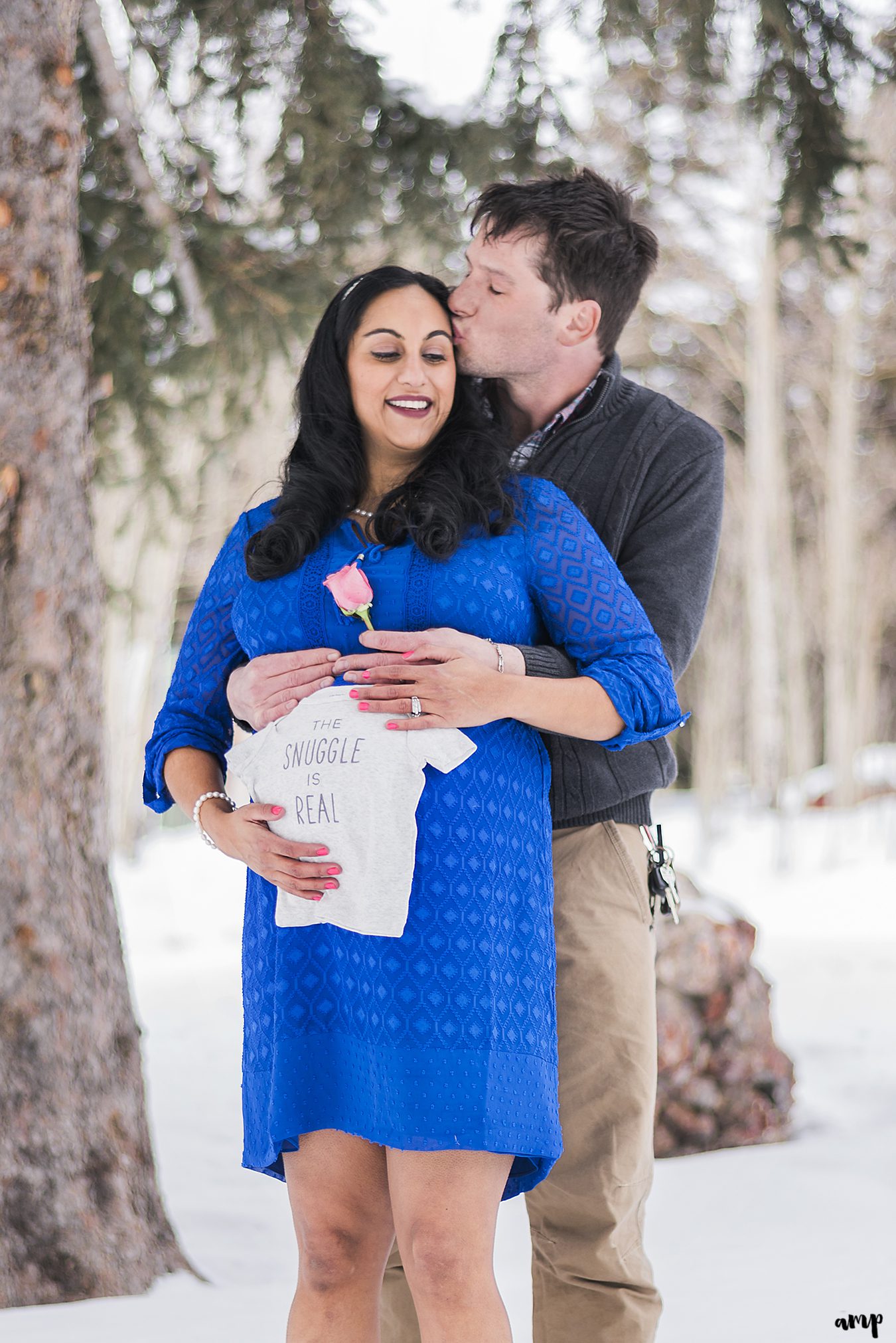 Expecting couple snuggle with a onesie reading "The Snuggle is Real"