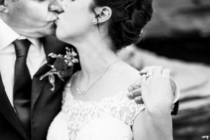 Black and white photo focused on wedding rings while couple kiss