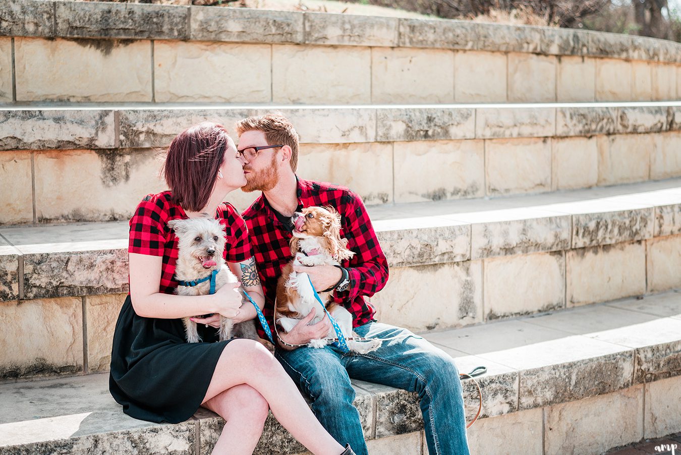 Ben and Courtnee kiss while holding their dogs along the riverfront