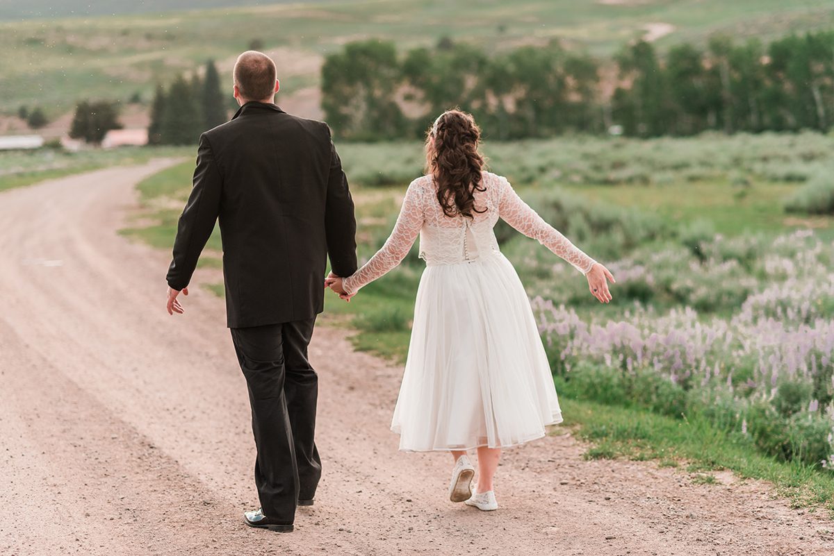 Bride and groom walking down a dirt road at sunset at Rolling R Ranch near Meeker