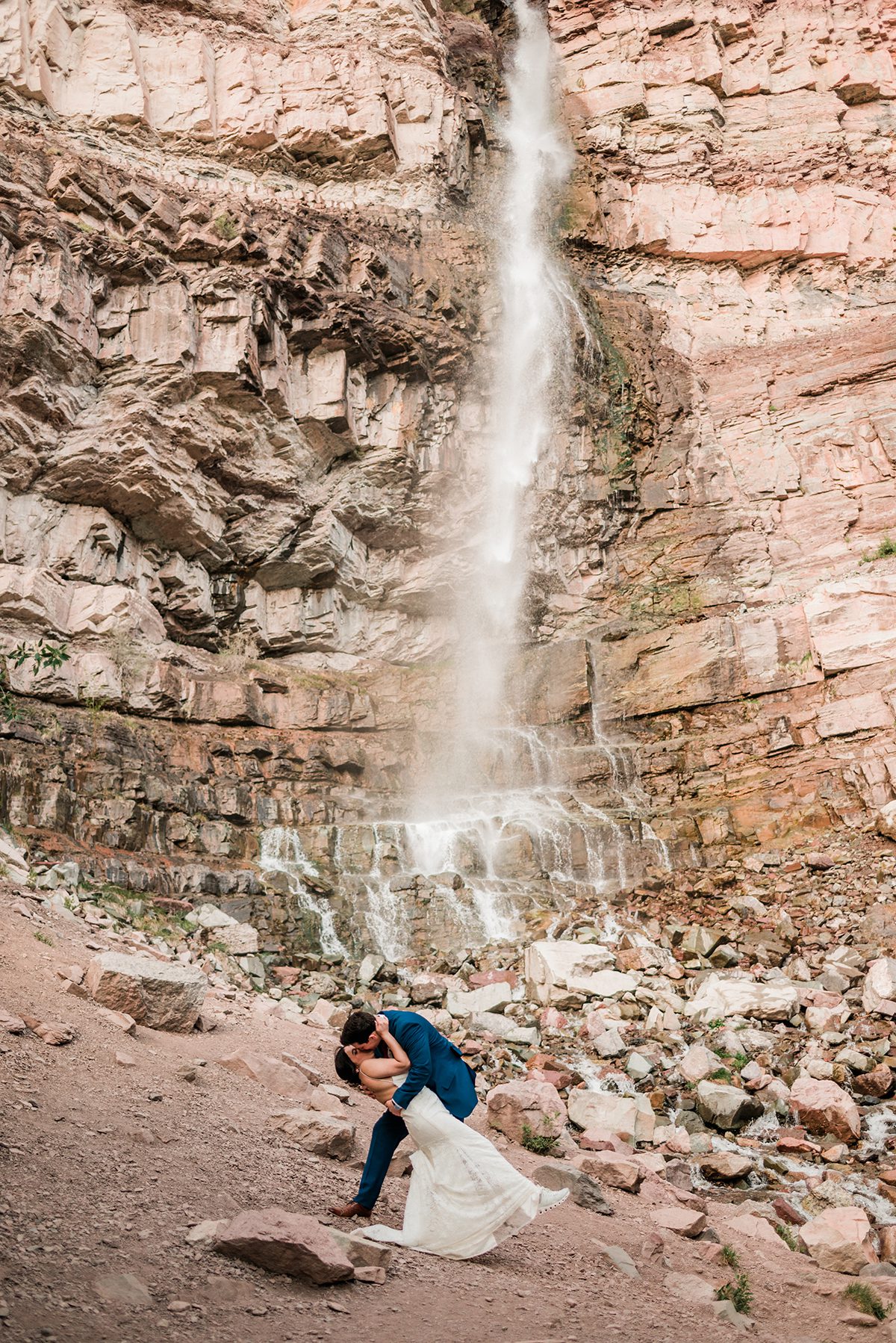 andrea and mckade share a kiss in front of the waterfall in ouray