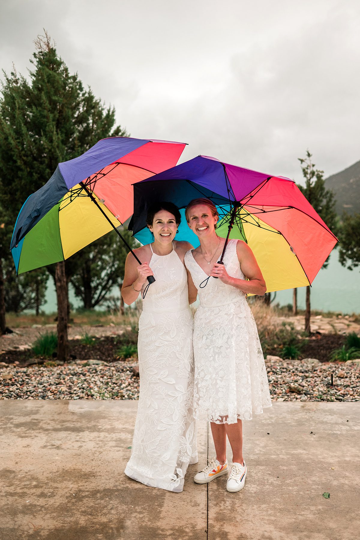 Two brides pose in the rain with rainbow umbrellas| Rainy Wedding at Vista View Events